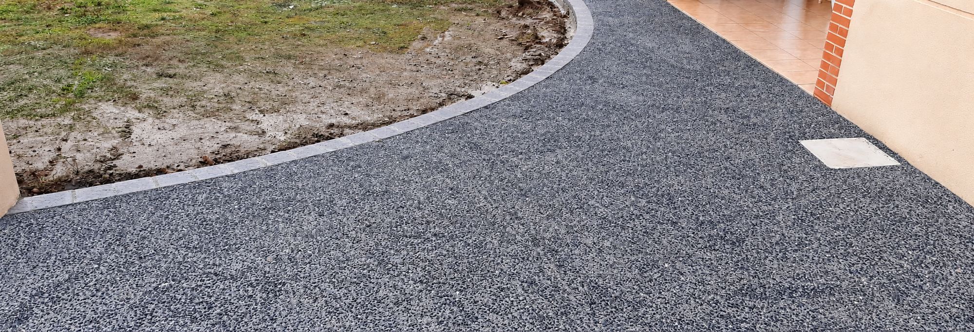 Allée en enrobé gris avec bordure de pavés qui longe la maison en courbe