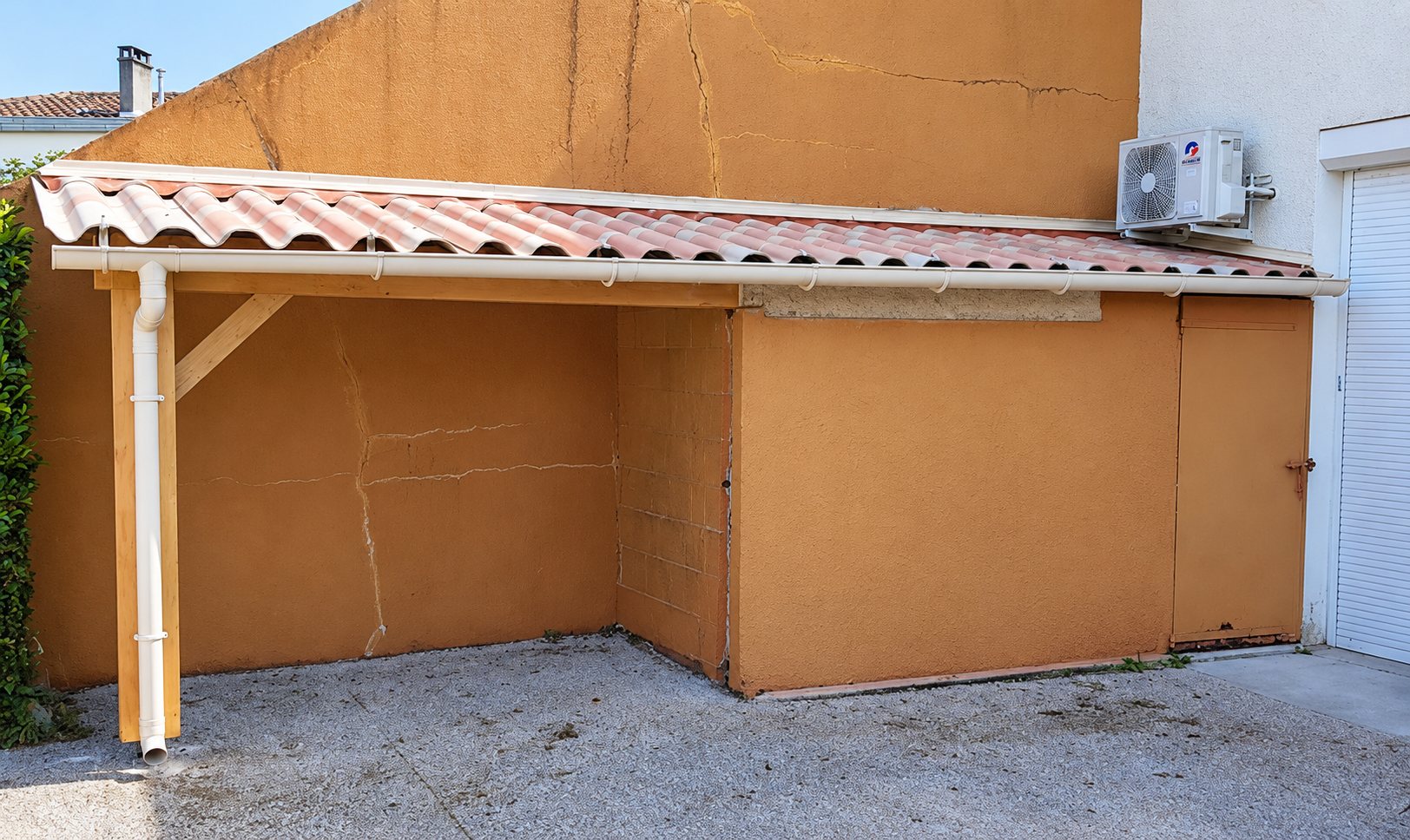 Auvent en bois avec toiture de tuiles ondulées contre un mur orange