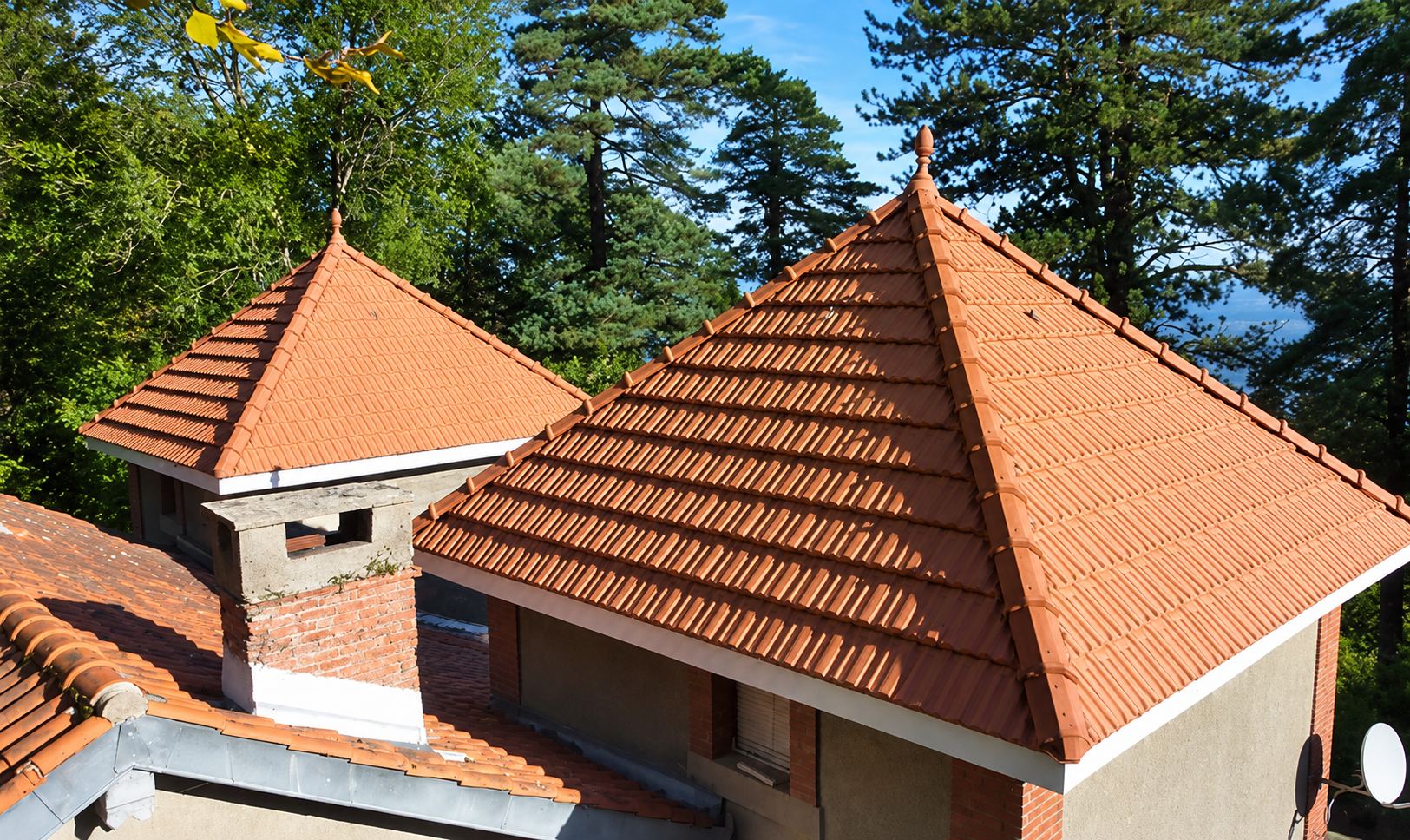 Toitures en tuiles rouges à quatre pans, avec une cheminée en brique, au milieu des pins